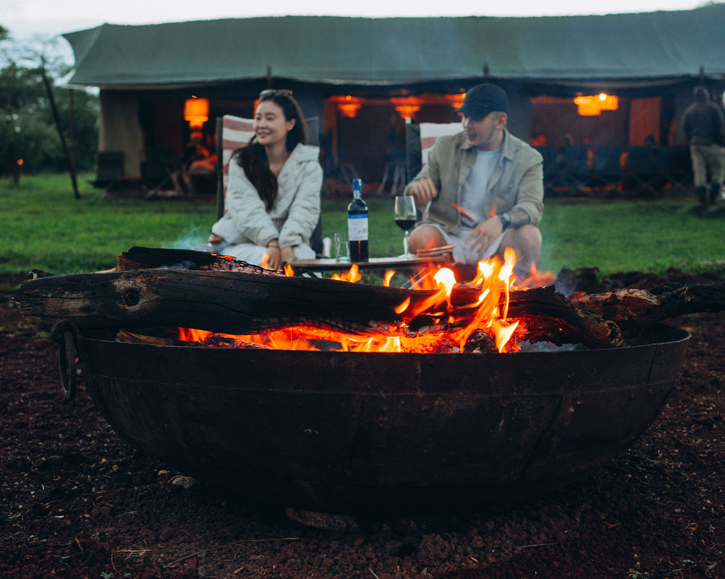 Guests beside a blazing firepit outside a lantern-lit tented camp