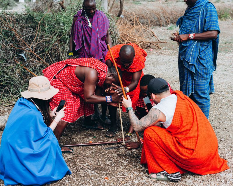 Maasai hosts demonstrating traditional fire-making to guests